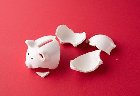 Broken whiter ceramic piggy bank in pieces on red surface