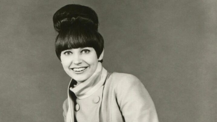 Black-and-white portrait of a young woman with a beehive hairstyle smiling at the camera.